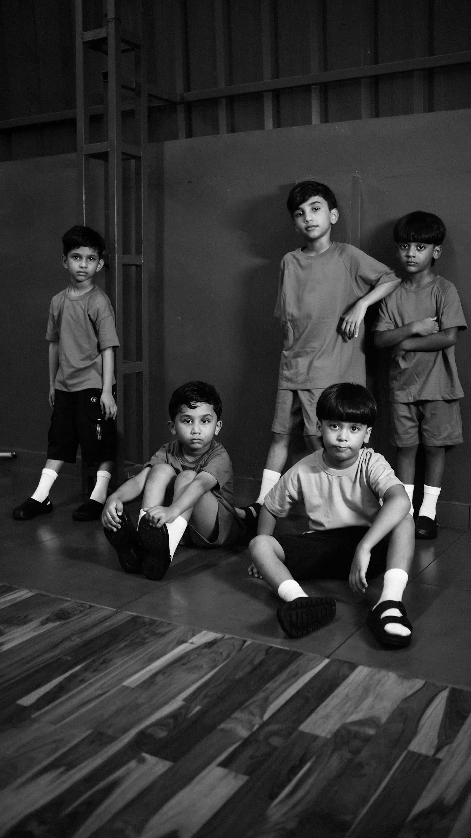 Black and white photo of five young boys in matching outfits by hadlad on a wooden floor.