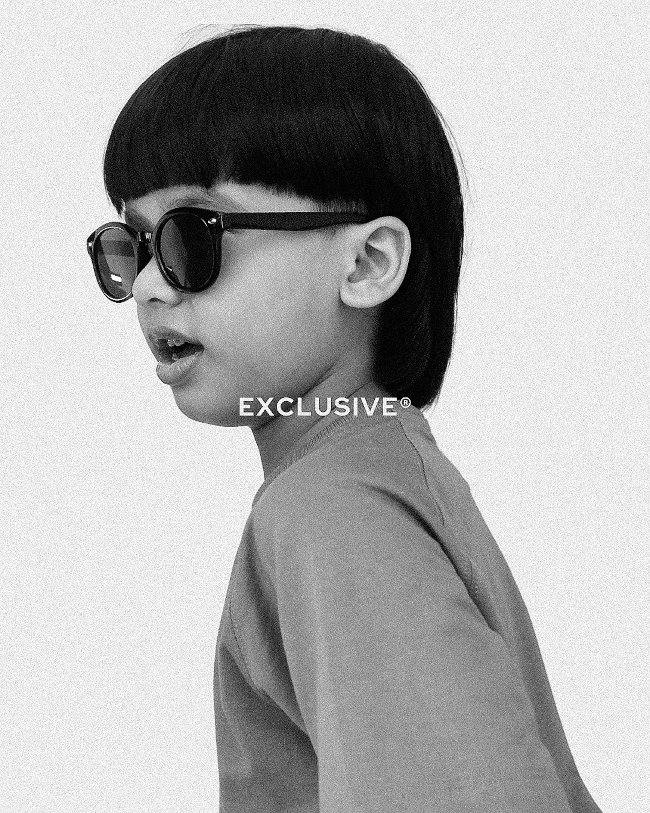 Black and white photo of a child wearing sunglasses with 'EXCLUSIVE' text.
